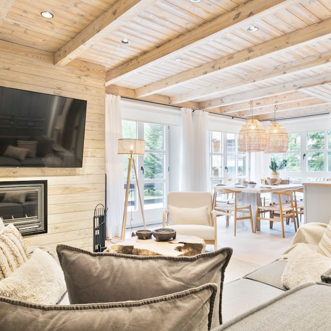 Baqueira 1500 - 1 Baqueira Beret alojamiento - Apartamento Viento - A cozy open-concept living area with a large sectional sofa, mounted TV, fireplace, dining table, and kitchen with island. Wooden ceiling beams and large windows add warmth and natural light to the space.