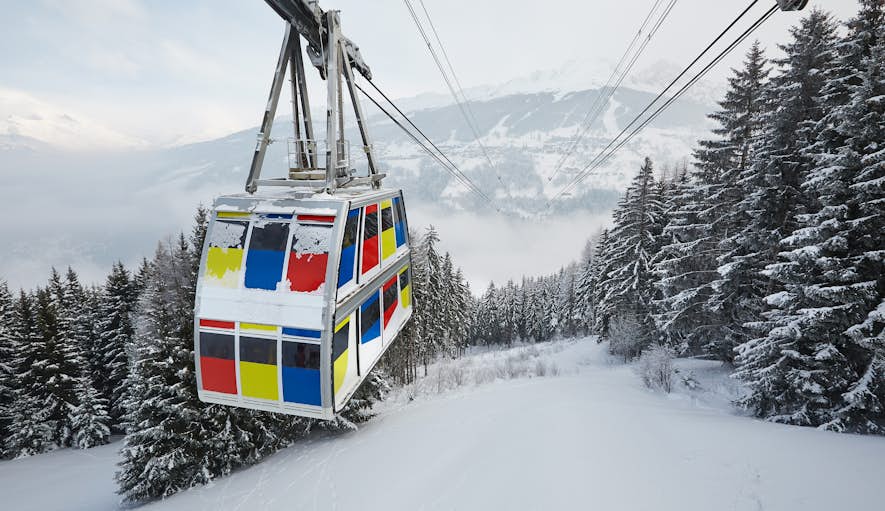A colorful cable car ascends a snow-covered mountain amidst pine trees, with foggy alpine scenery in the background.