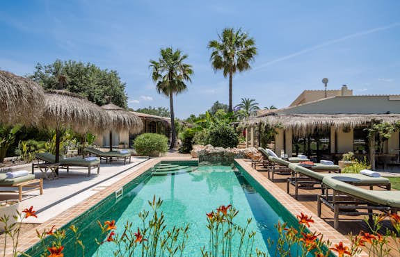 A swimming pool with lounge chairs and thatched umbrellas.