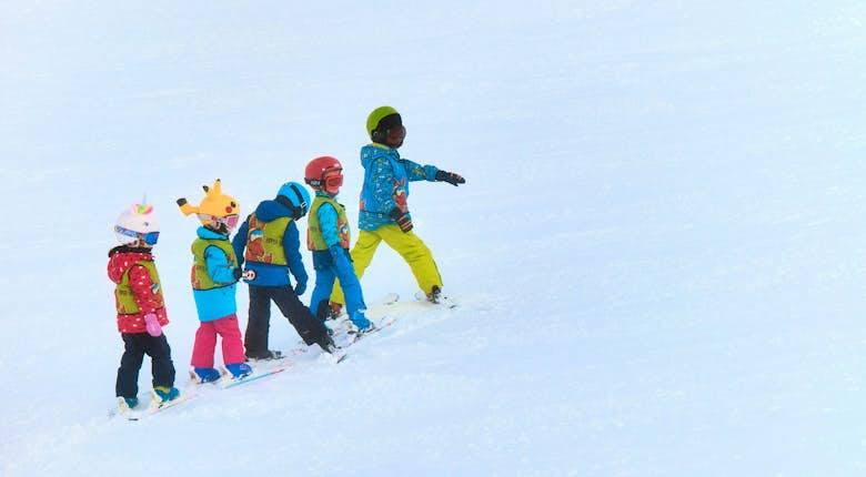 A group of children on skis on a snow covered slope.