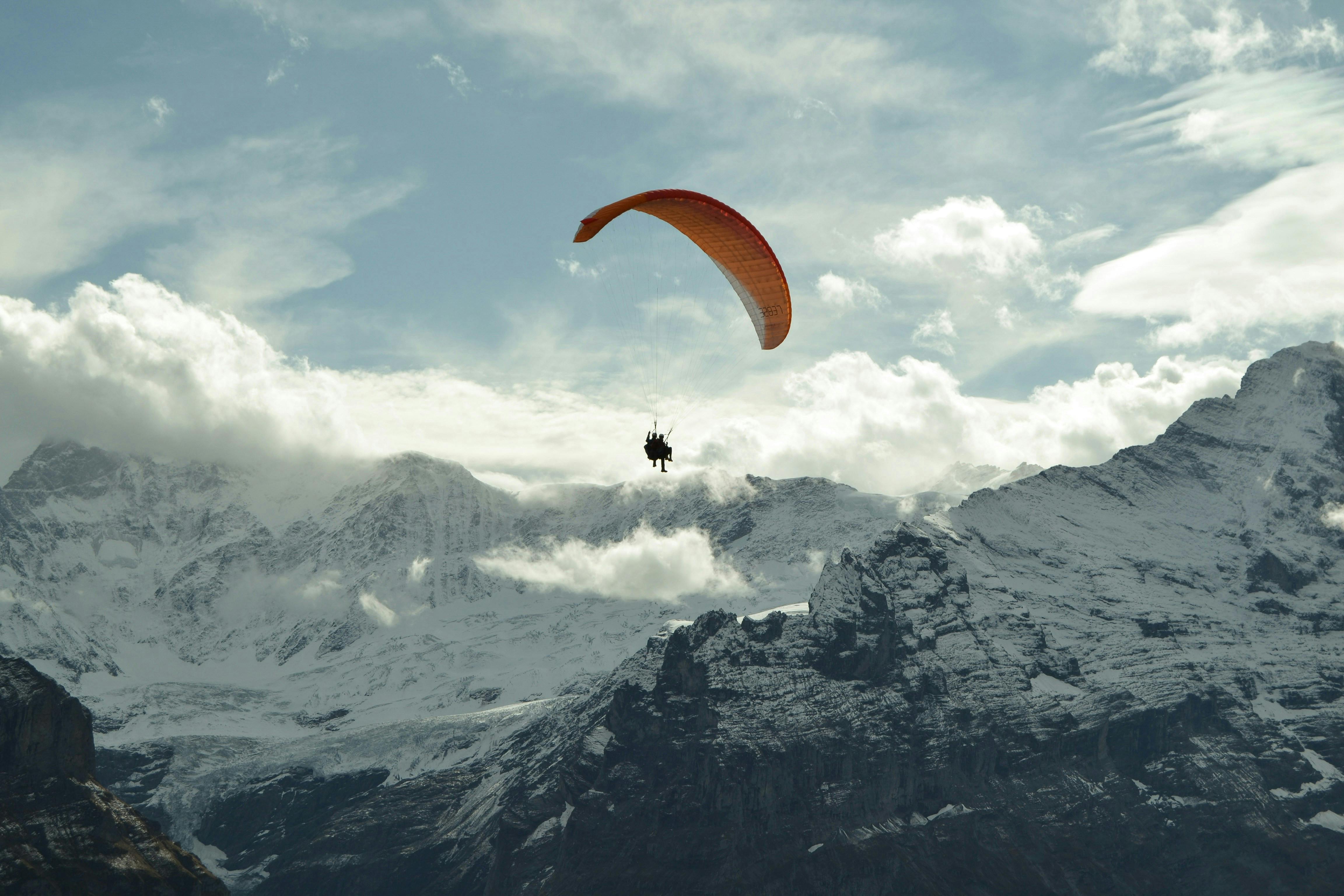 A person paragliding over a snow covered mountain.