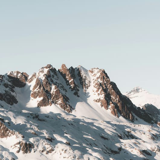 Skiers on snowy slopes with a backdrop of majestic mountains and clouds, with a small village visible below.