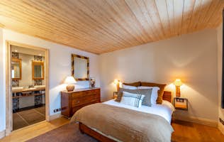 Courchevel 1850 - 3 Courchevel location - Chalet Salix - Cozy bedroom with a wooden ceiling, a double bed, a dresser with a lamp, and an attached bathroom visible in the background.