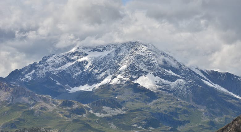 A mountain range with snow-covered peaks and green valleys under a partly cloudy sky.