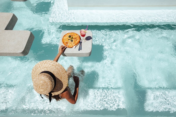 Une dame se détendant dans une piscine avec un verre et une pizza