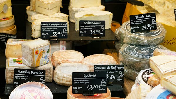 A variety of cheeses on display with price tags, including Brie, Maroilles, and Bleu de Loire, arranged on a counter in a market setting.