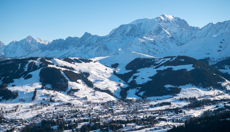 Praz-sur-Arly from hot-air balloon Snow-covered mountain landscape with a town nestled in the valley, surrounded by forests and clear blue skies.