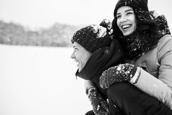 Un homme portant une femme sur son dos vêtu de vêtements d'hiver dans la neige