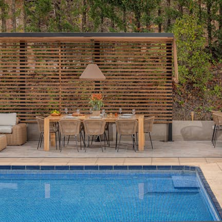 An elegant outdoor patio with a dining area and pool, featuring wooden privacy screens and modern furniture.