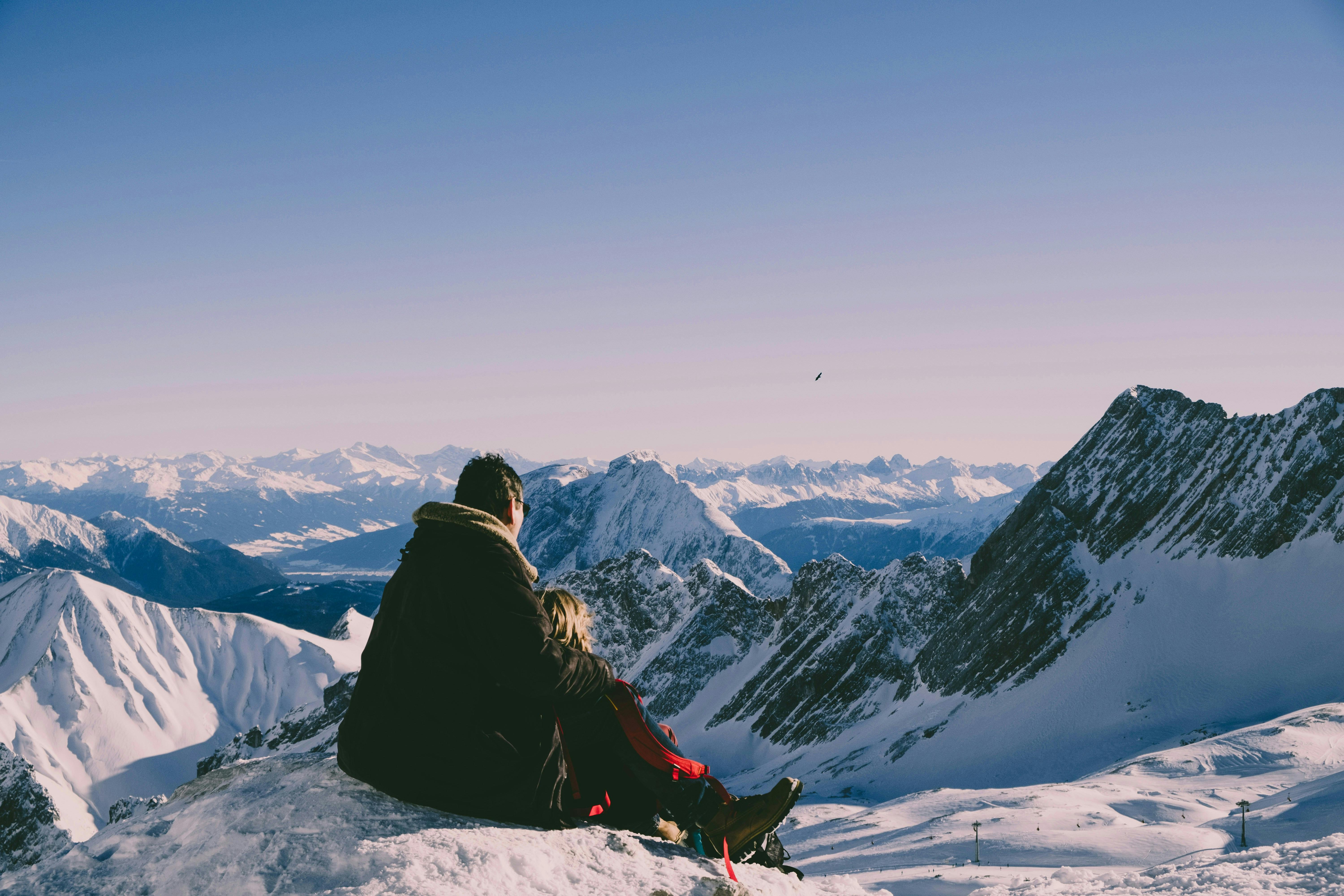 Two people sitting on top of a snow covered mountain.
