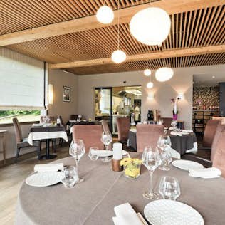 Modern restaurant interior with elegantly set tables, plush seating, wooden ceiling slats, and large spherical pendant lights.