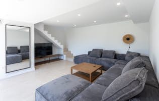 Costa Brava accommodation - Apartment Onada - Modern living room with a large gray sectional sofa, wooden coffee table, TV under staircase, wall mirror, and minimalist decor.