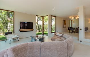 Saint-Tropez - 2 Verbier alojamiento - Villa Noon - Modern living room with a contemporary sofa facing a wall-mountain television between bright windows displaying lush plants outside