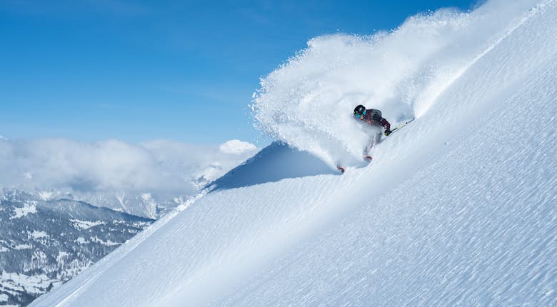 A skier carves down a steep snowy mountain, spraying snow in the air