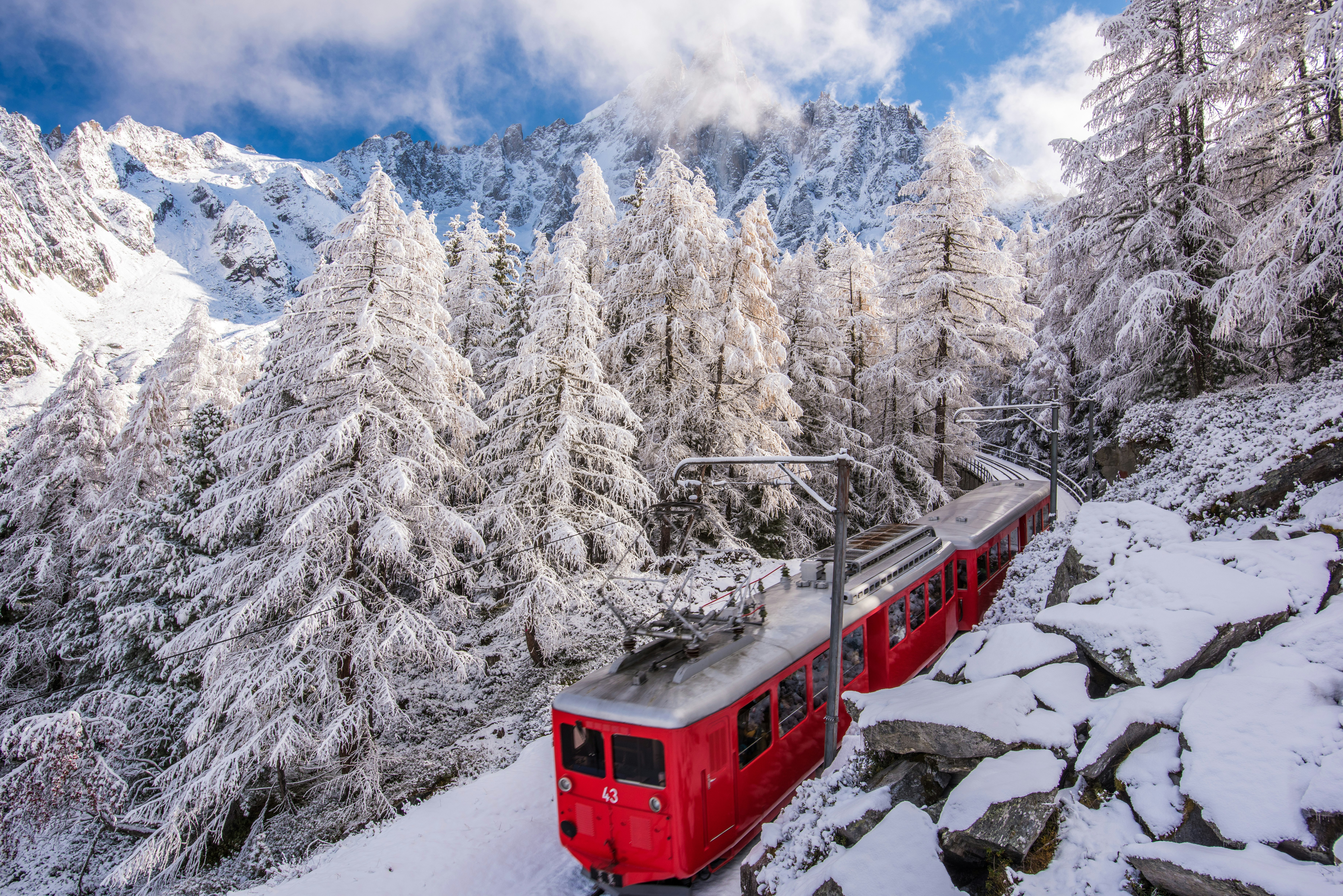 French Ski Resorts Near Geneva | Emerald Stay A bright red train on tracks surrounded by snow covered pine trees and mountain peaks