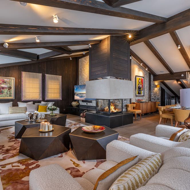 Morzine alojamiento - Chalet Coquelicot - Chalet Coquelicot, Courchevel Morzine alojamiento - Chalet Coquelicot - Spacious living room with modern decor, featuring white sofas, geometric tables, a central fireplace, and exposed wooden beams on the ceiling.