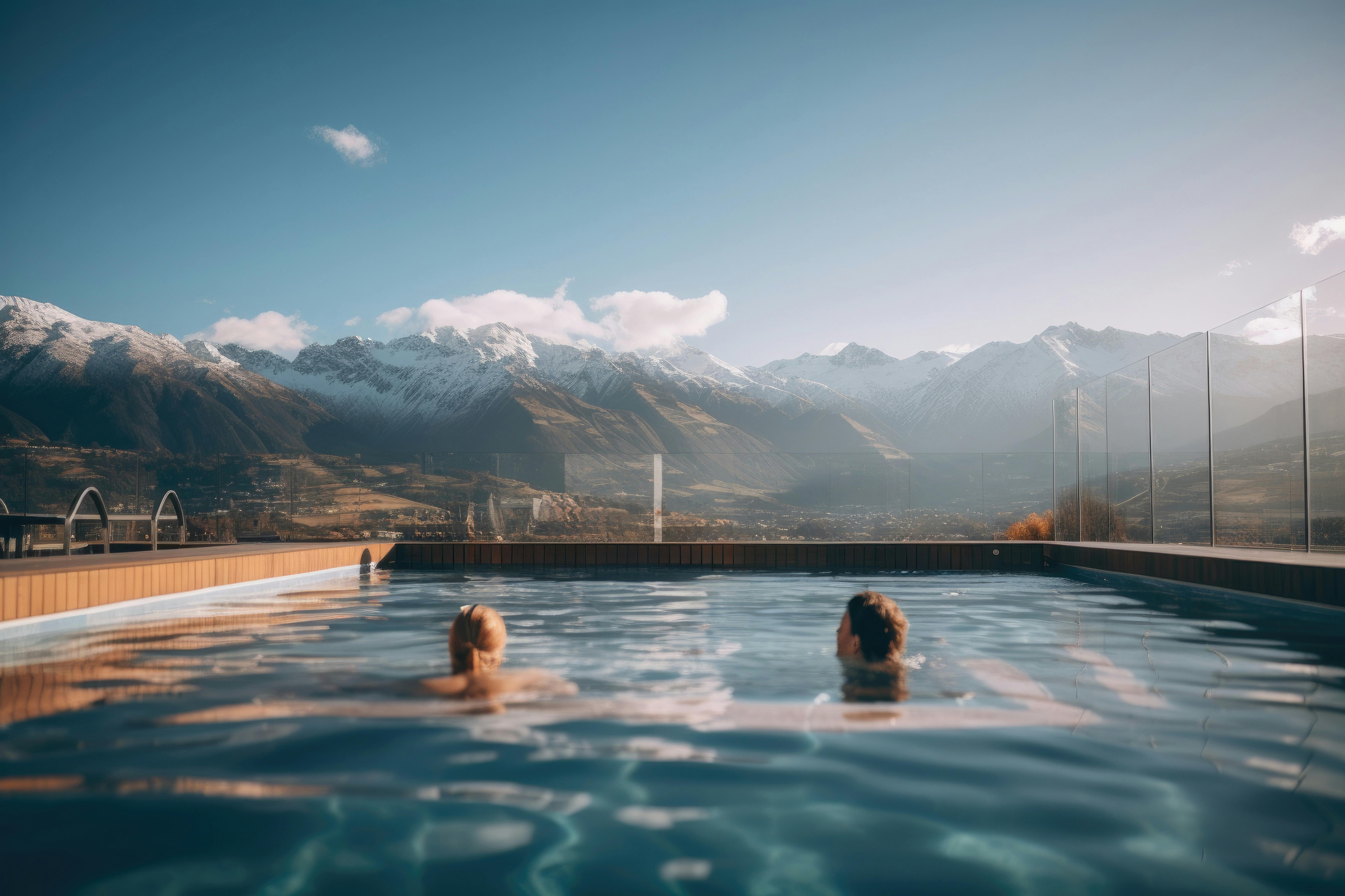 Two people swimming in a pool with mountains in the background.