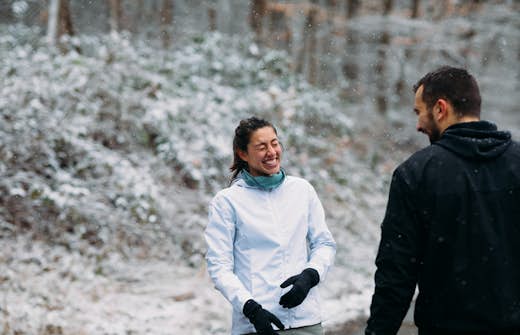 Two people in the snow Two people in winter clothing laugh together outside on a snowy day, with a forest backdrop.