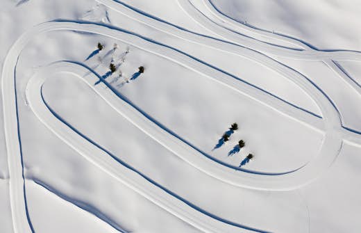 Aerial view of winding roads in a snow-covered landscape with a few sparse trees.
