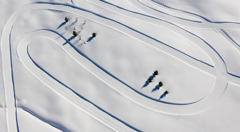 Aerial view of winding roads in a snow-covered landscape with a few sparse trees.