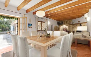 Mallorca accommodation - Villa Alyvos - Modern kitchen with a wooden dining table, white chairs, exposed ceiling beams, and pendant light, viewed from one end of the table.