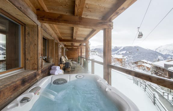 A hot tub on a balcony overlooking snowy mountains.
