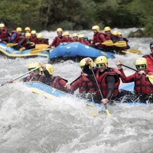 Two groups of people in helmets and life jackets enthusiastically navigate whitewater rapids in inflatable rafts.
