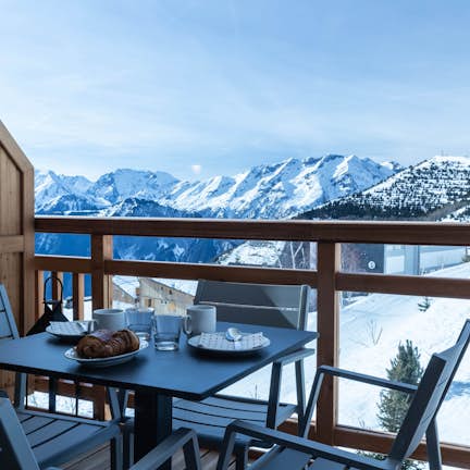 A table and chairs on a balcony overlooking snowy mountains.