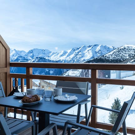 Apartment Juglans A table and chairs on a balcony overlooking snowy mountains.